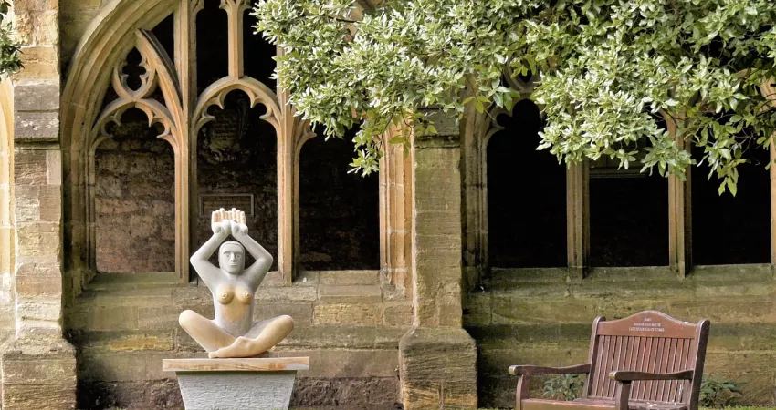 Sculpture of a sitting woman with hands raised to the sky in New College Cloisters