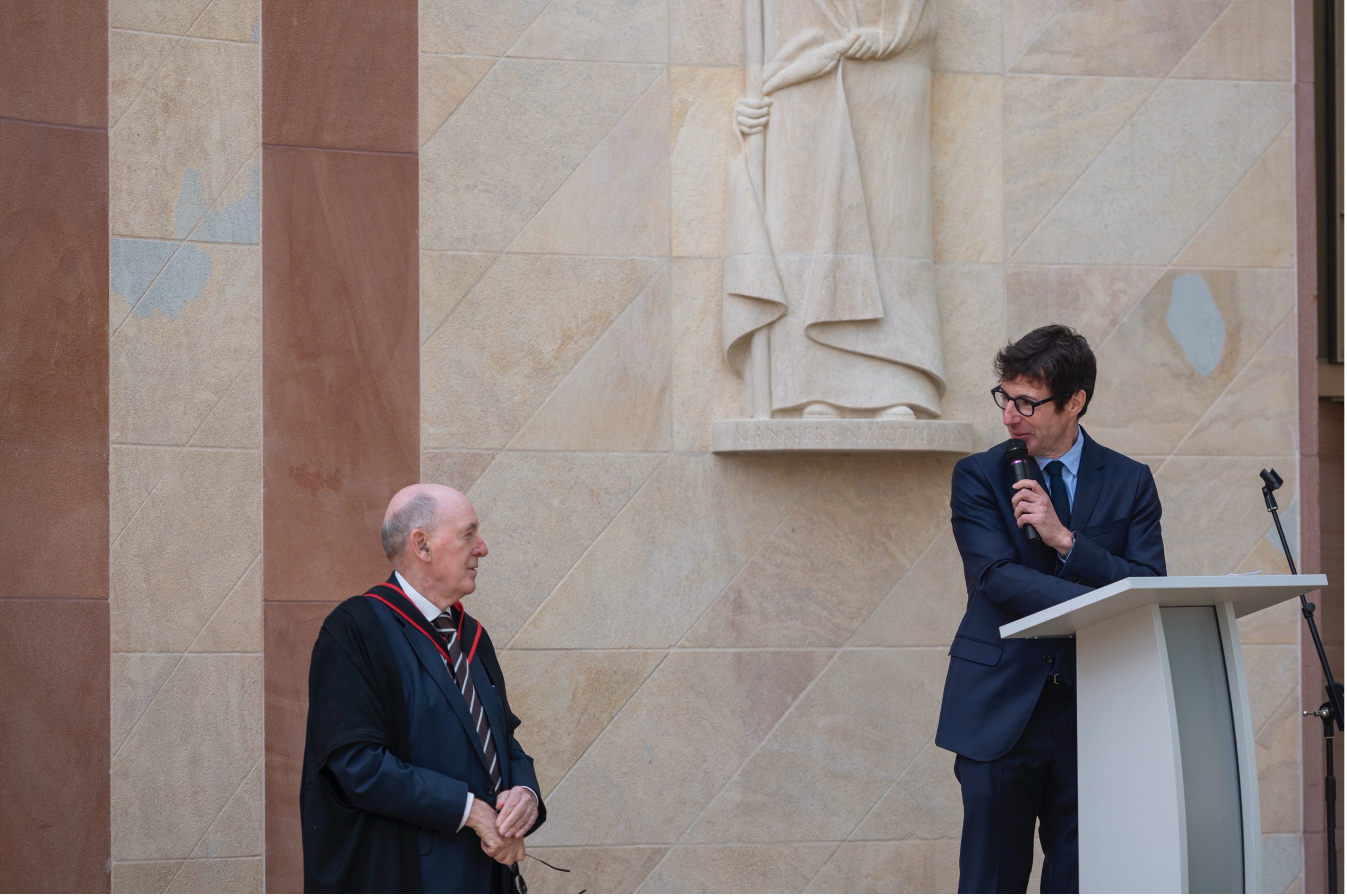 Chris Gradel and the Warden give speeches under the William of Wykeham statue