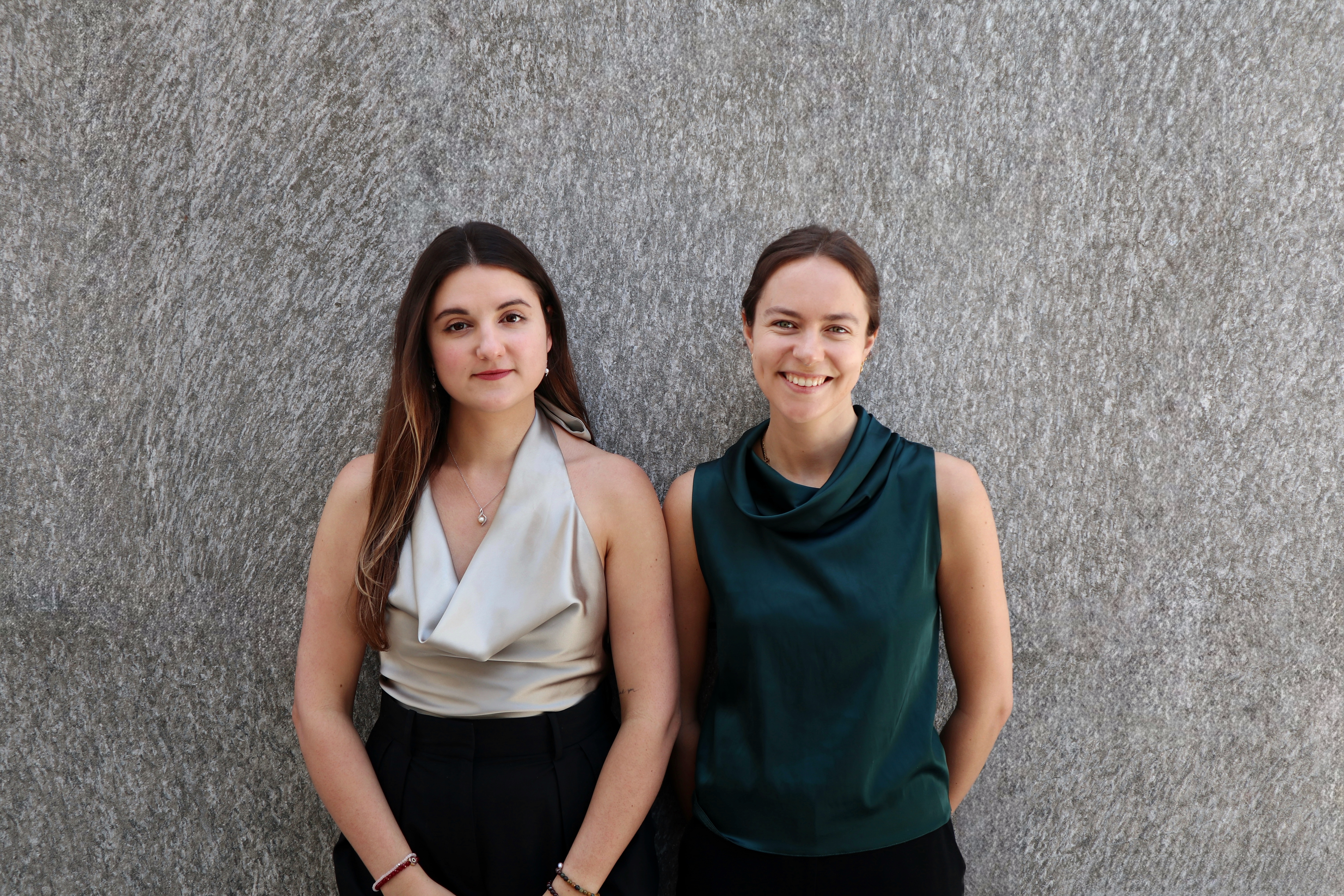 Anastasia and Laura stand together against a grey wall.