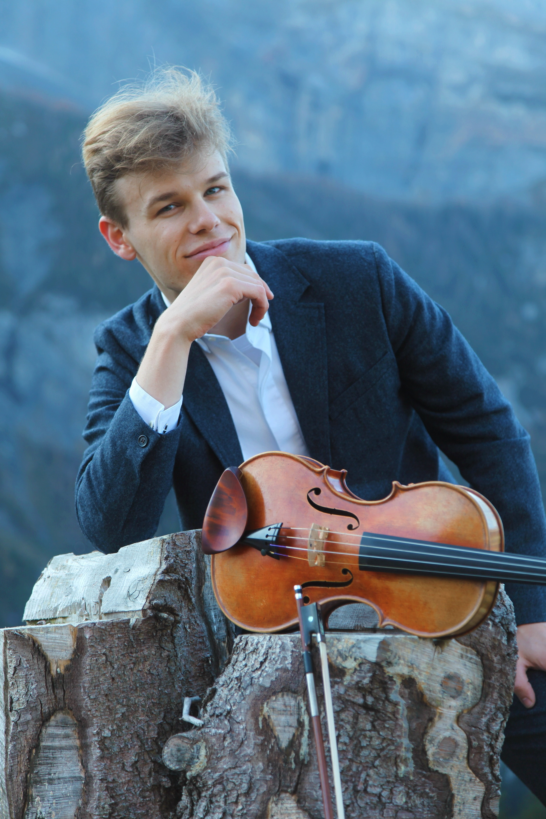 Joel Munday poses with his violin against a mountainous background.