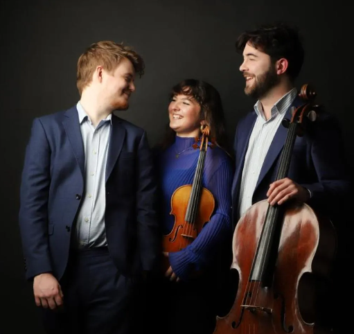 Trio Casella smile at each other, holding their instruments, against a plain black backdrop