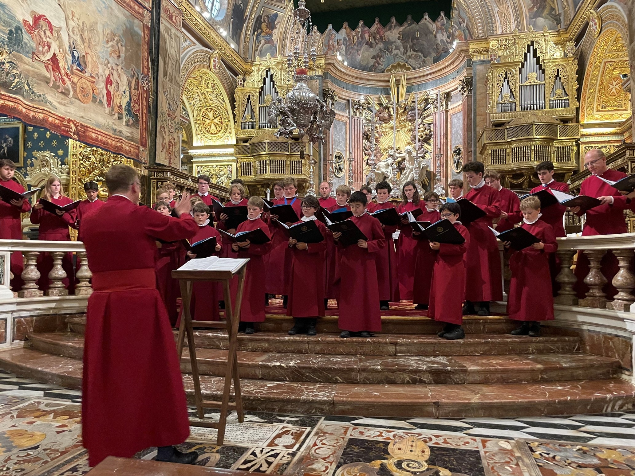 A choir wearing red robes, performing in an elaborately decorated church