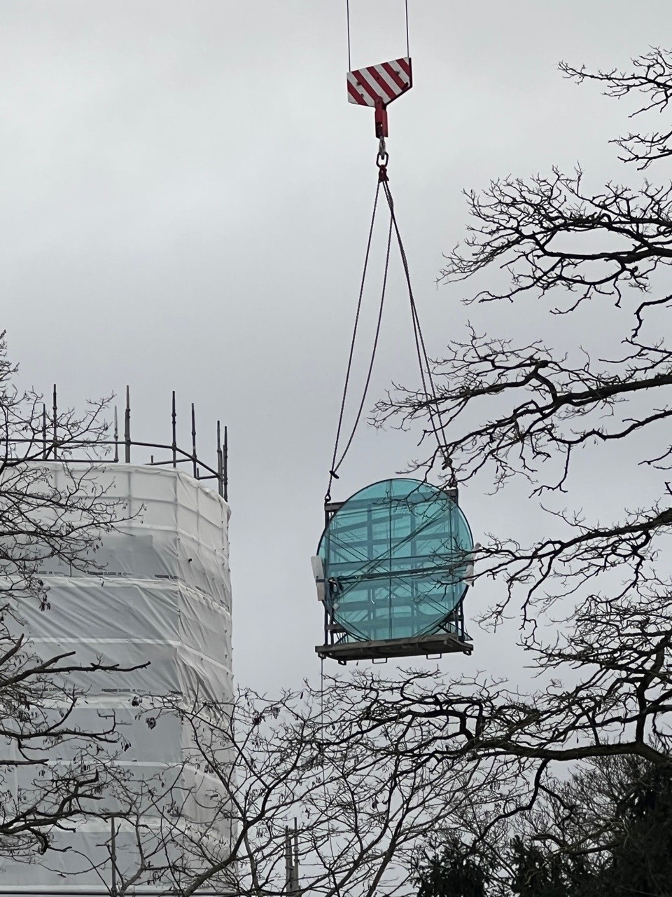 Crane lifting a large circular window up to the top of a nearby tower