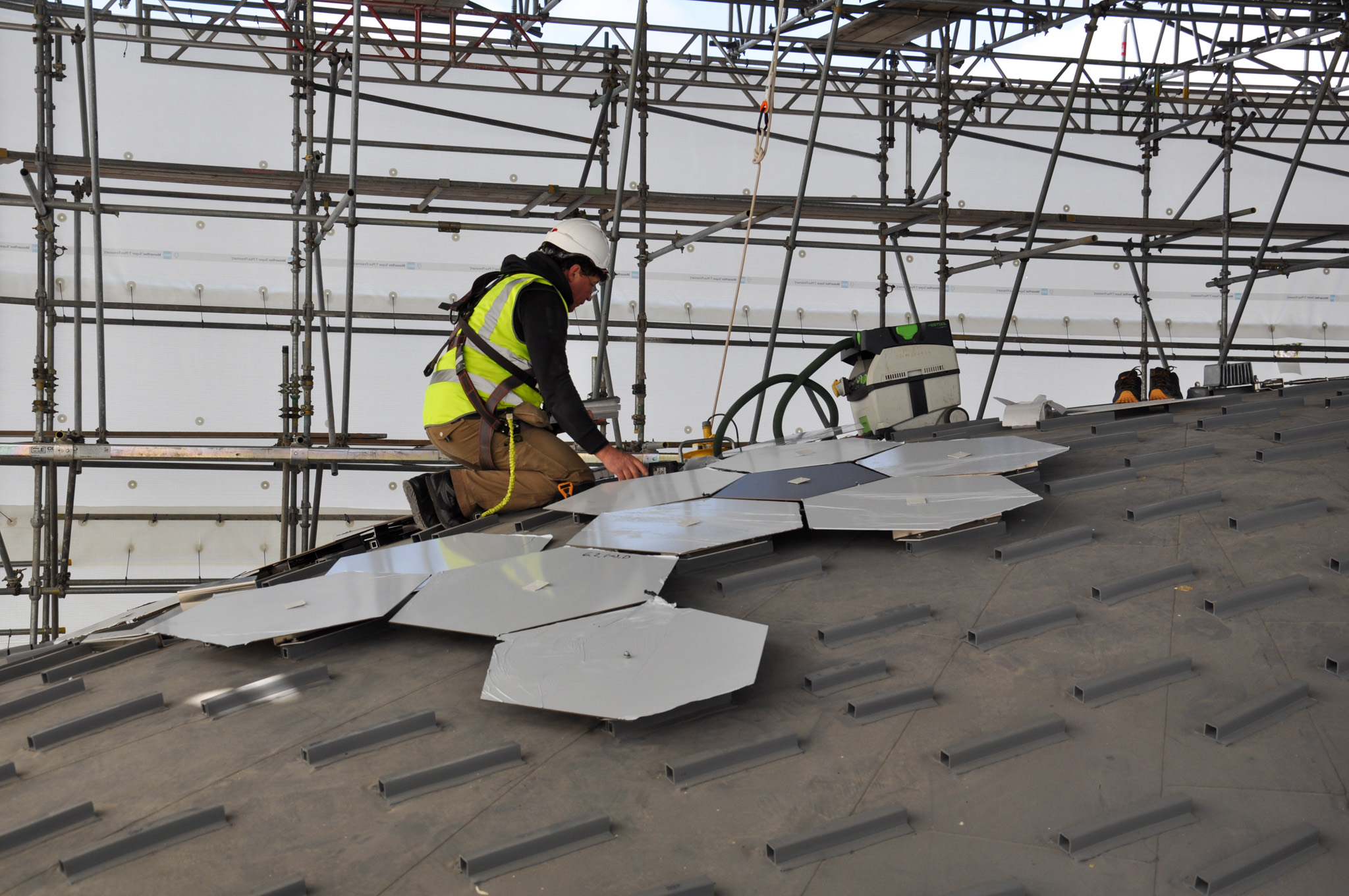 A man in high-vis laying aluminium roof tiles