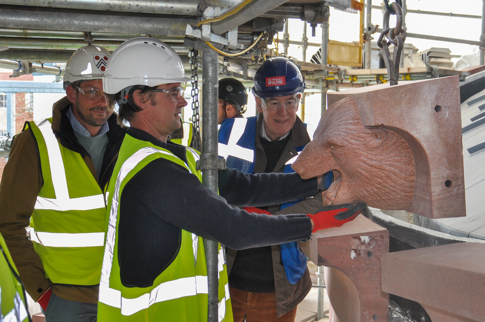 Three people in hard hats and high-vis vests alongside a gargoyle of a polar bear's head