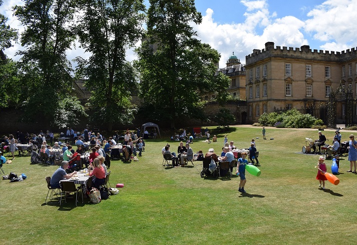 People sat around tables on a large expanse of grass with trees in the background