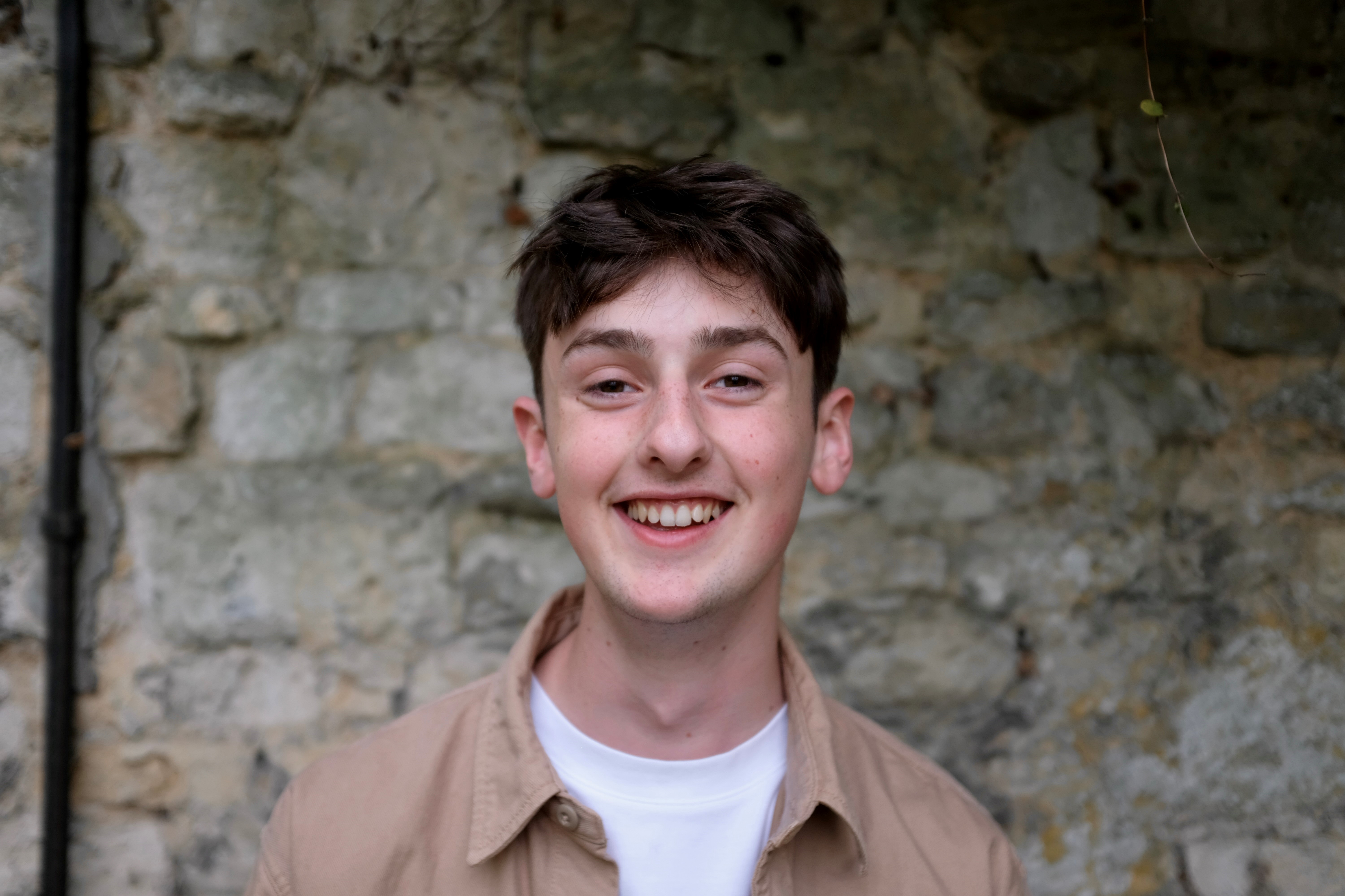 Luke in New College gardens in front of a brick wall