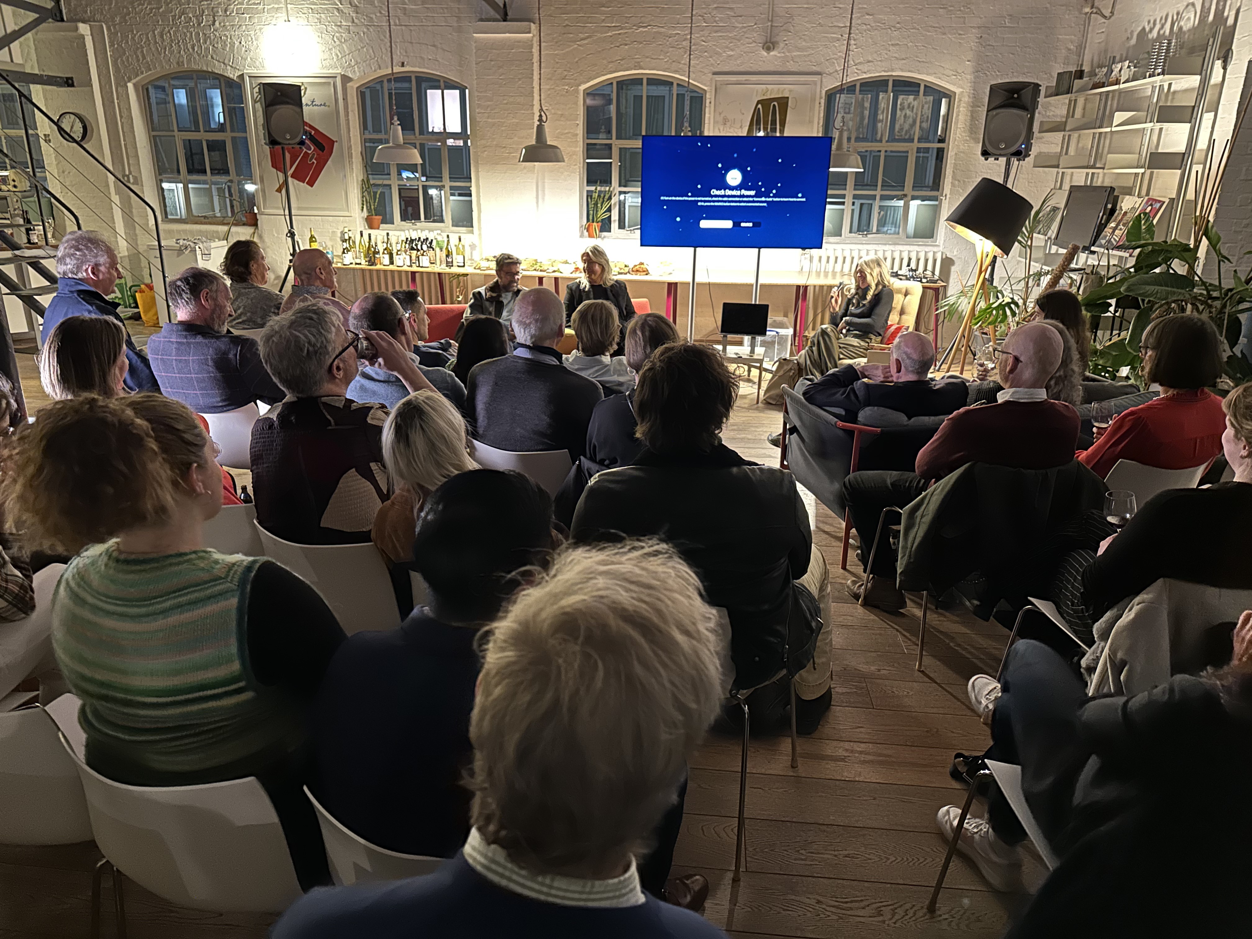 A three-person panel talk to an audience with a screen and windows in the background