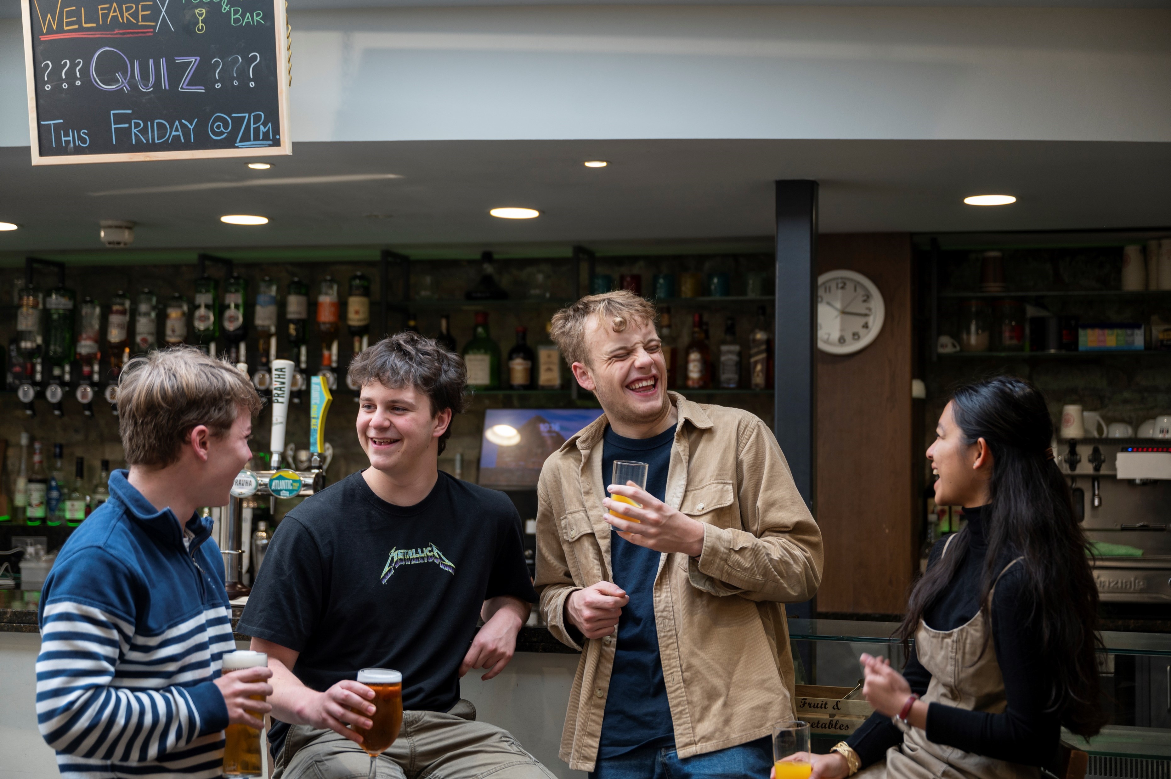 Four students chat and enjoy drinks in the New College Bar