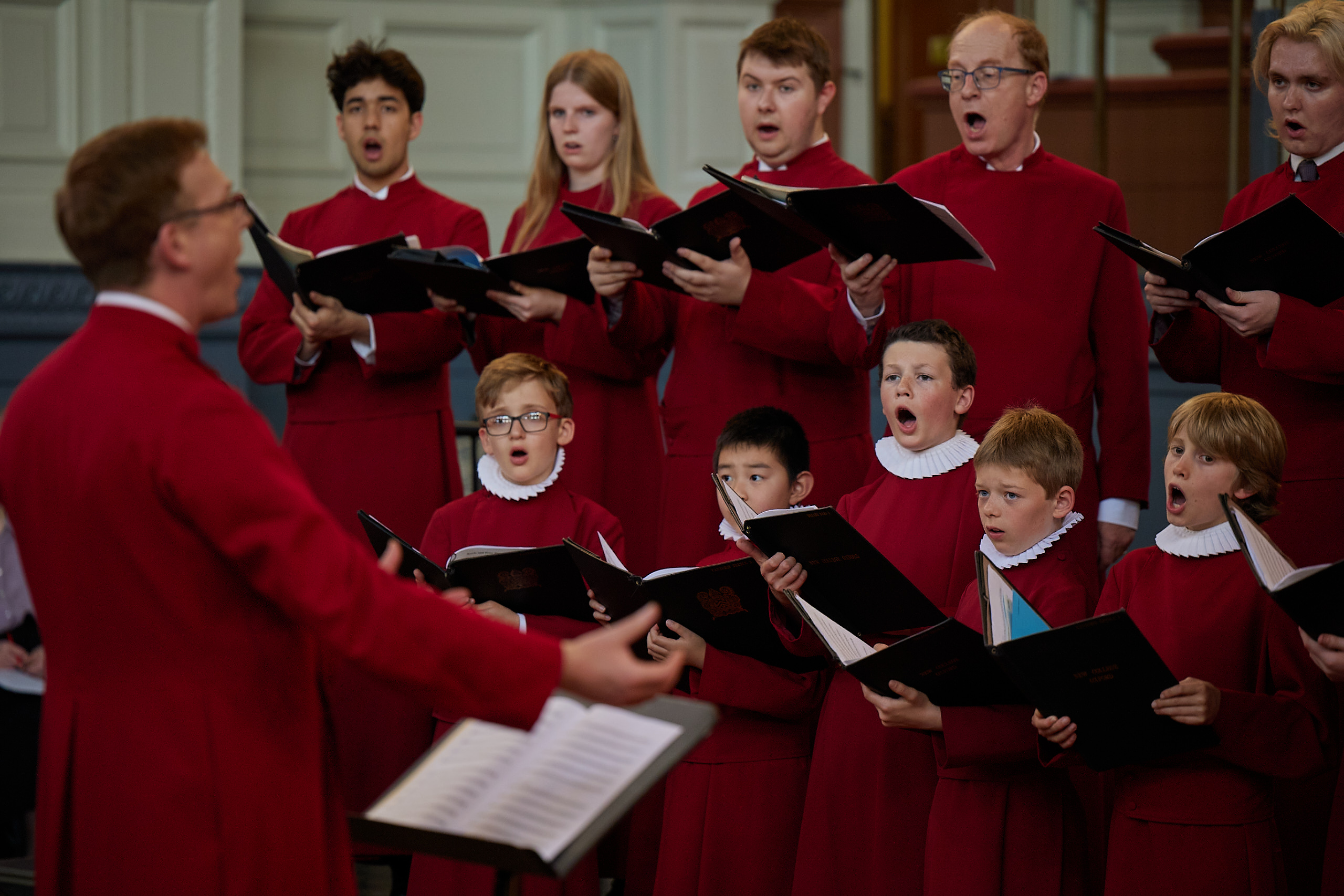 A choir singing dressed in red, with conductor in the foreground