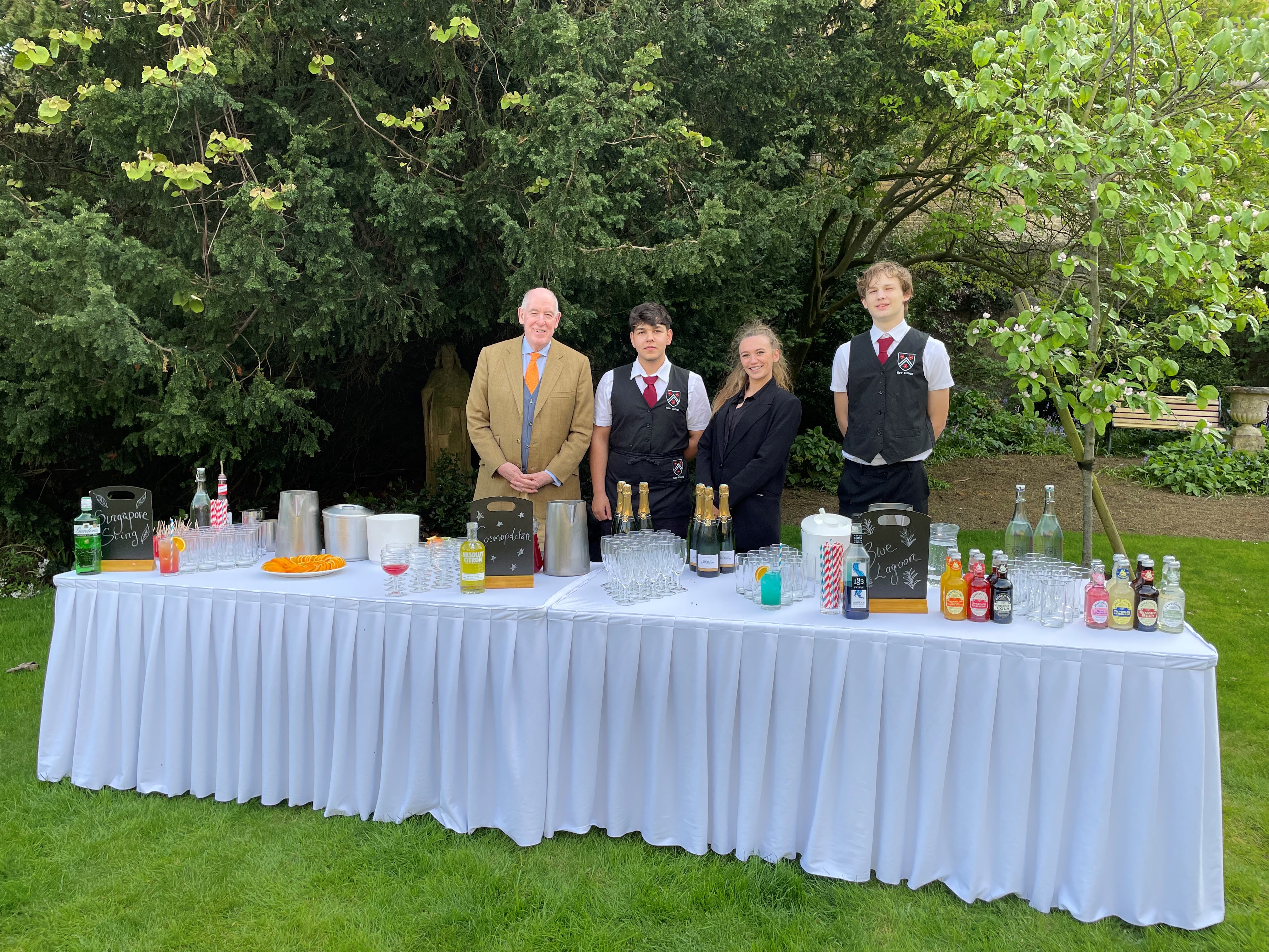 Four people standing behind a table with lots of drinks on