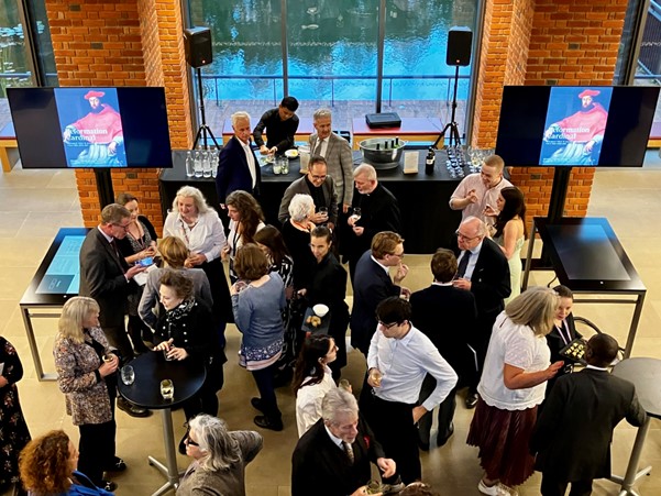 Picture taken from above the launch event. On the screens are posters of the exhibition.