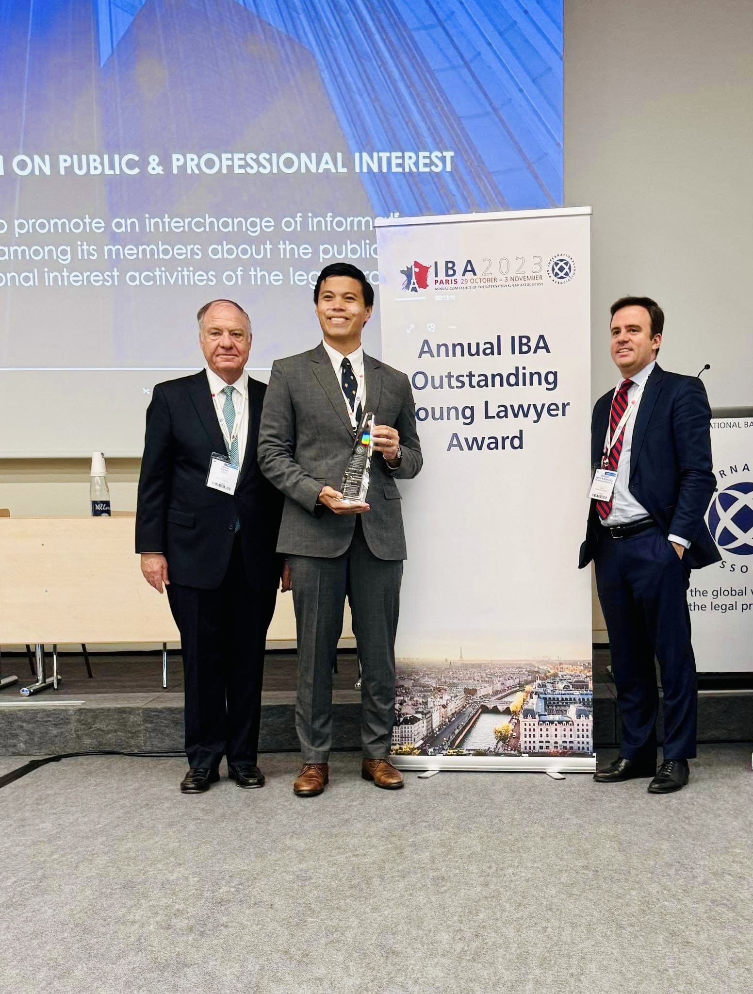 Raphael Pangalangan receives his award. He stands by two colleagues in front of a roller banner which says "Annual IBA Outstanding Young Lawyer Award"