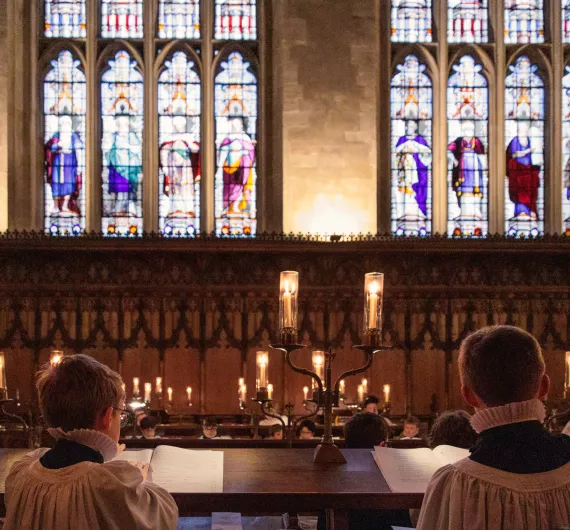 Two choristers sat in a chapel with stained glass windows