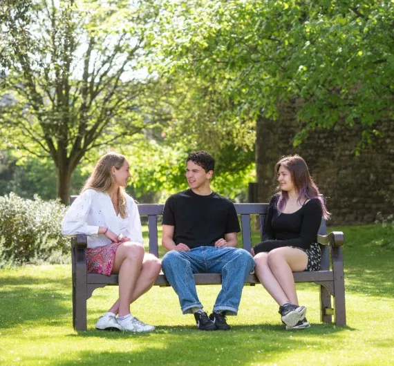 Three students sit on a bench in New College gardens