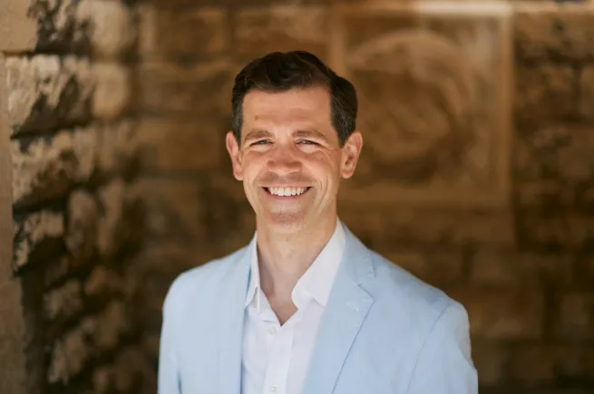 Christian C. Sahner, wearing a pale blue suit, standing against a brick wall