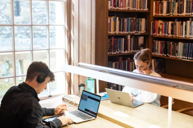 Two students on laptops study in the library