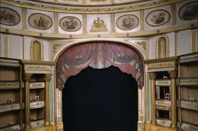 A golden stage from the view of an audience member. On top of the stage is a red curtain.