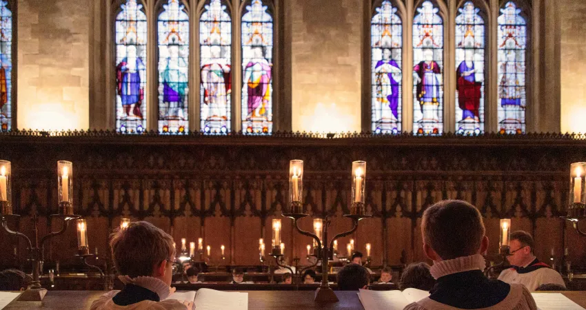 Two choristers sat in a chapel with stained glass windows