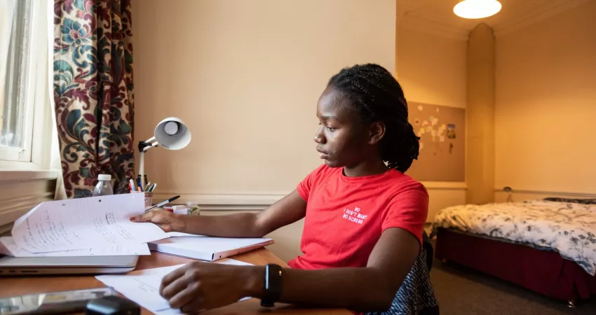 Student sat at her desk, with double bed in the background