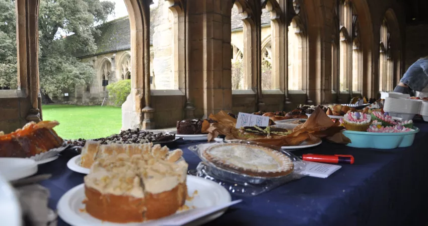 A selection of cakes on a blue tablecloth, with the Cloisters behind