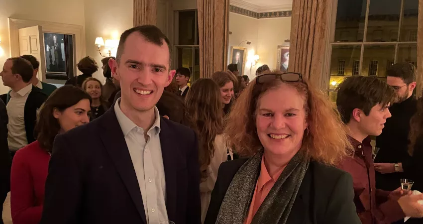 A man and woman standing smiling at the camera, with lots of other people in the background