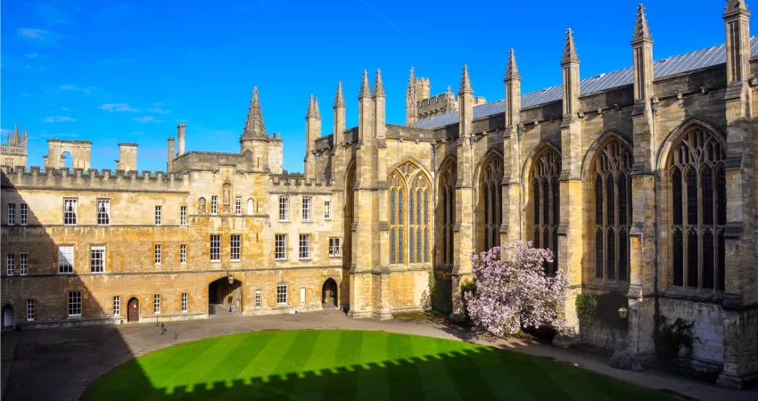 Medieval quadrangle with a blooming magnolia, shadows of crenellations on the lawn, and blue sky