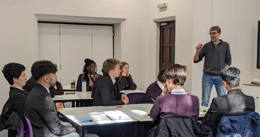 School students sitting around tables receiving a talk from a professor