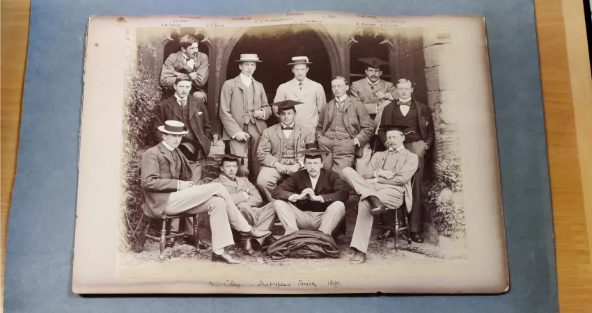 Black and white photo of men in suits and hats posed in cloisters