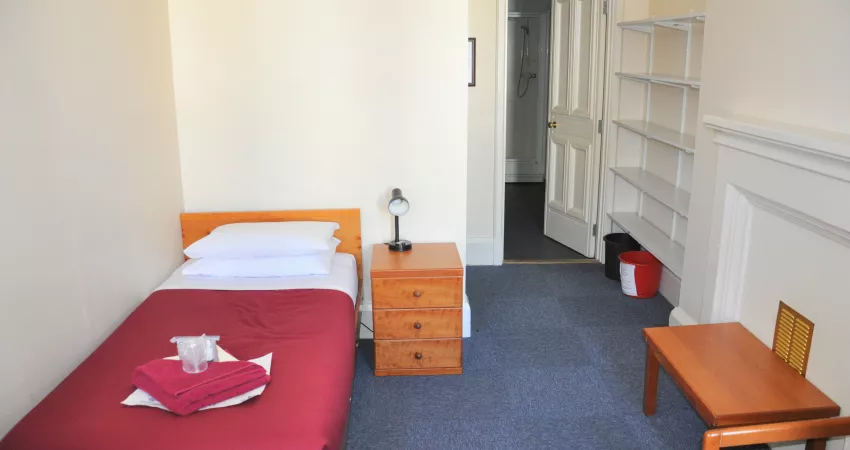 Student room with single bed, bedside table and shelves, leading to en suite bathroom