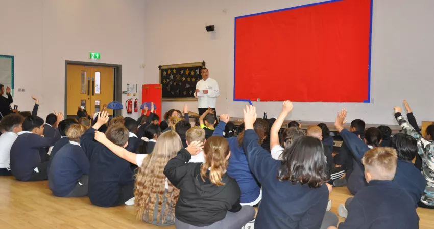 Students sat, many with their hands raised, as a chef stands at the front of the group