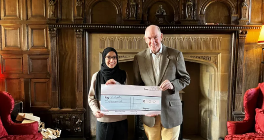 Hibah stands with the Warden holding a large cheque