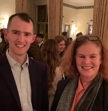 A man and woman standing smiling at the camera, with lots of other people in the background
