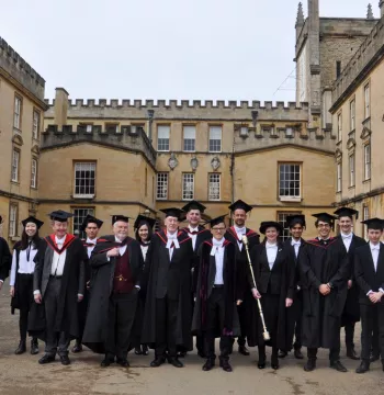 A group of people in formal gowns smiling at the camera; gothic 3-sided quad in the background