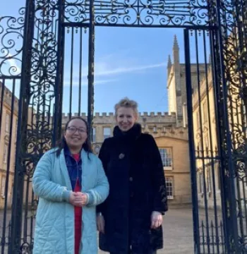 Two women smile at the camera, with an elaborate iron screen and Georgian quad in the background