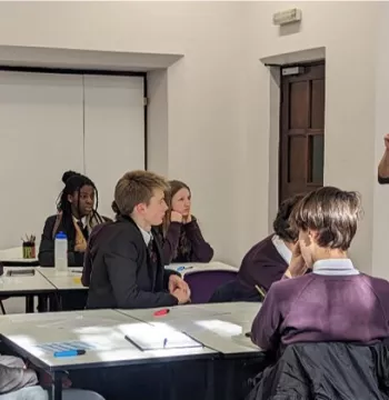School students sitting around tables receiving a talk from a professor