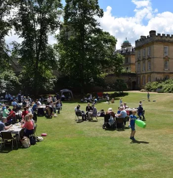 People sat around tables on a large expanse of grass with trees in the background