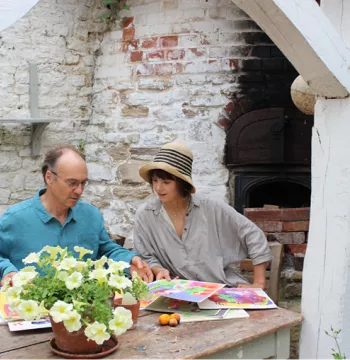 Julian and Gabriella sit beside a wooden table and look at their paintings