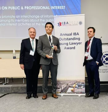 Raphael Pangalangan receives the Outstanding Young Lawyer award. He stands by two colleagues in front of a roller banner which says "Annual IBA Outstanding Young Lawyer Award"