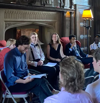 The Warden stands with the MCR Salon speakers in front of an audience in the lodgings