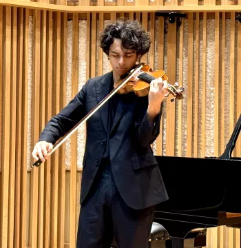 Man with dark hair in black suit plays the violin